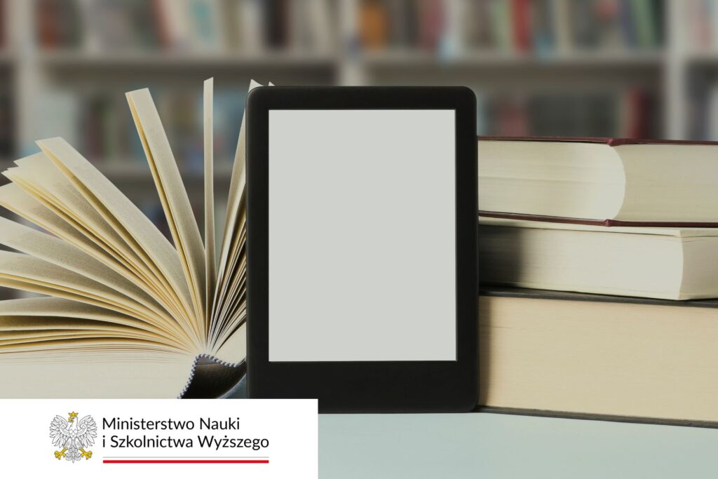 Na pierwszym planie czytnik e-booków oparty o książki/doktoraty. W tle półka z książkami
