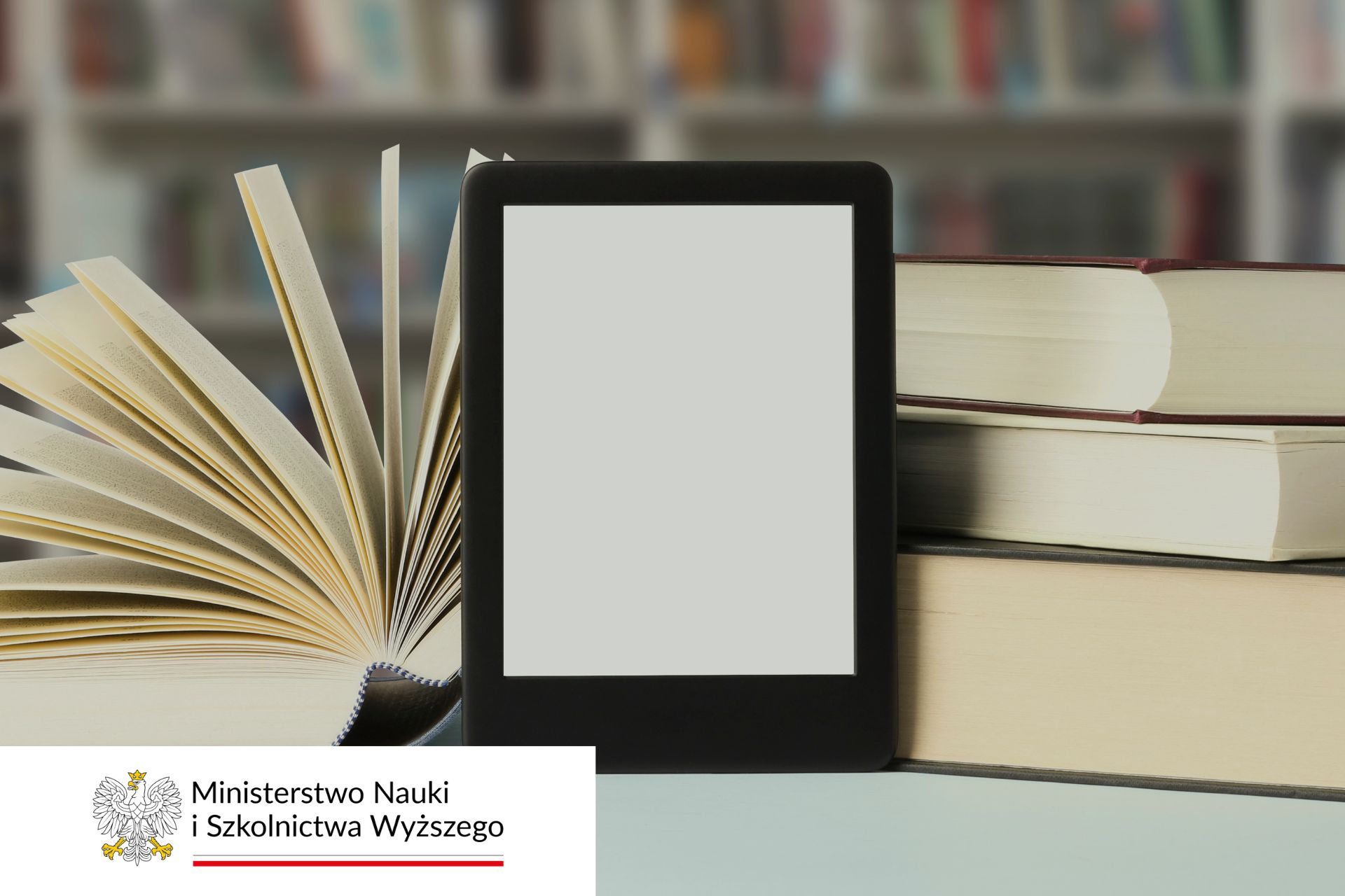 Na pierwszym planie czytnik e-booków oparty o książki/doktoraty. W tle półka z książkami