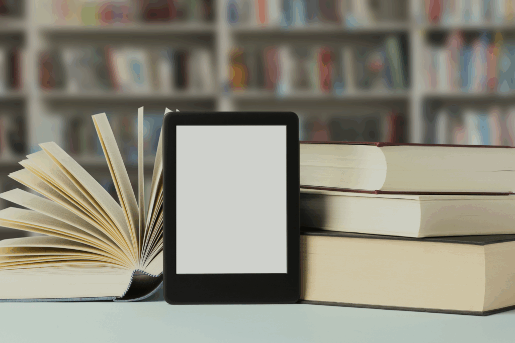 Na pierwszym planie czytnik e-booków oparty o książki/doktoraty. W tle półka z książkami