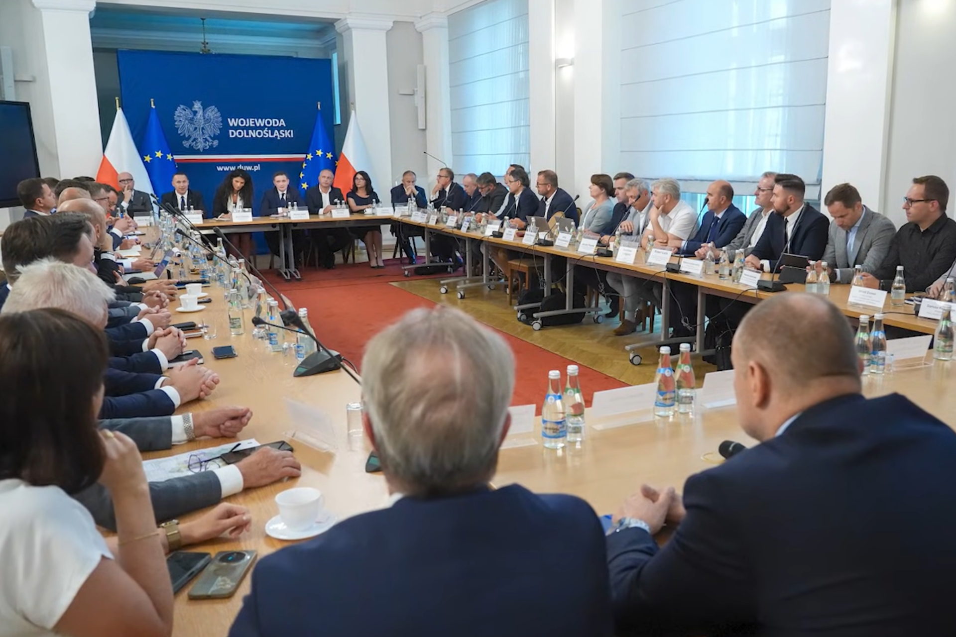 Zdjęcie z rozmów w Dolnośląskim Urzędzie Wojewódzkim we Wrocławiu dotyczące TEEMA Technology Park w Miękini. Wielu ludzi siedzących przy stole na tle flag Polski i Unii oraz granatowego baneru z napisem Wojewoda Dolnośląski
