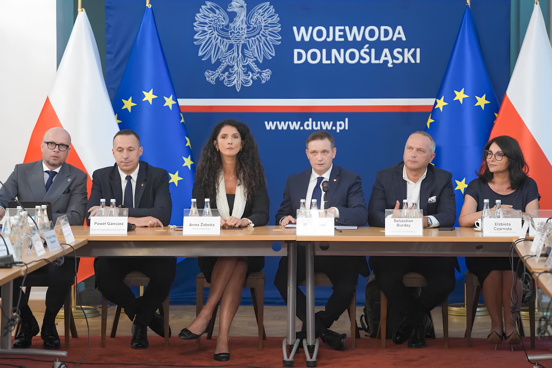 Zdjęcie z rozmów w Dolnośląskim Urzędzie Wojewódzkim we Wrocławiu dotyczące TEEMA Technology Park w Miękini. 6 osób siedzących przy stole na tle flag Polski i Unii oraz granatowego baneru z napisem Wojewoda Dolnośląski